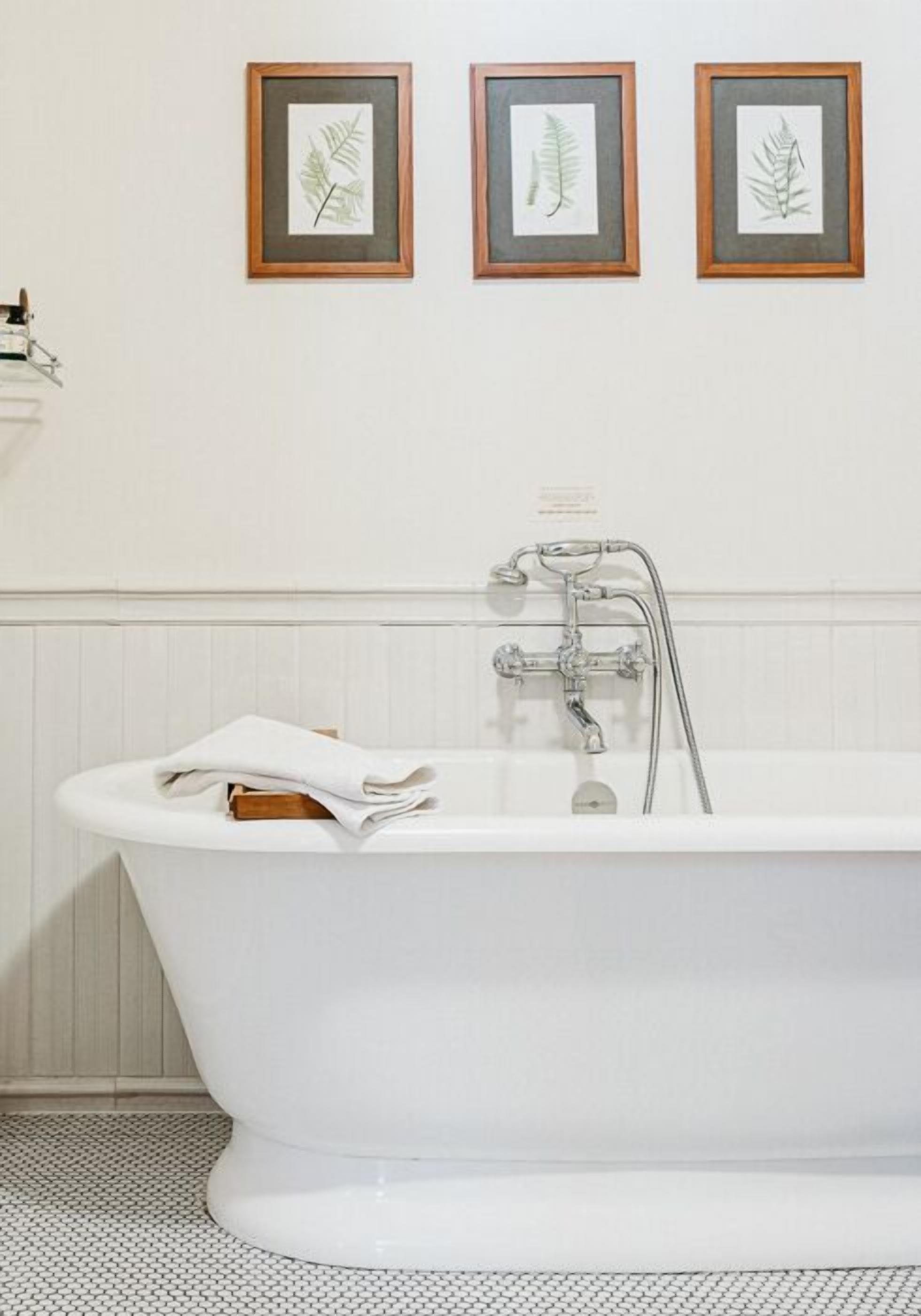 A bathroom with a white bathtub, a towel, and three framed botanical prints on the wall.