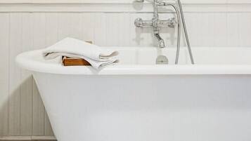 A bathroom with a white bathtub, a towel, and three framed botanical prints on the wall.