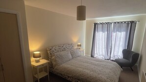 A bedroom with a bed, bedside lamps, a chair, and a window with curtains.