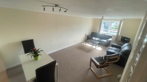A living room with a white table, a black sofa, a black armchair, and a small table with a plant.