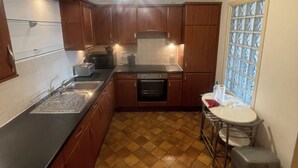 A compact kitchen with wooden cabinets, a black countertop, a small oven, and a window with frosted glass.