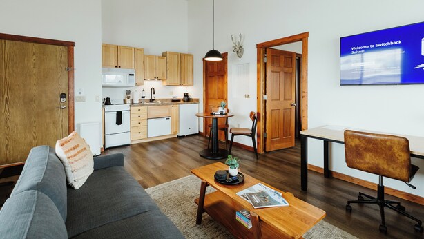 En moderne stue med sofa, sofabord og et fjernsyn, der viser 'Welcome to Switchback Suites!'.
