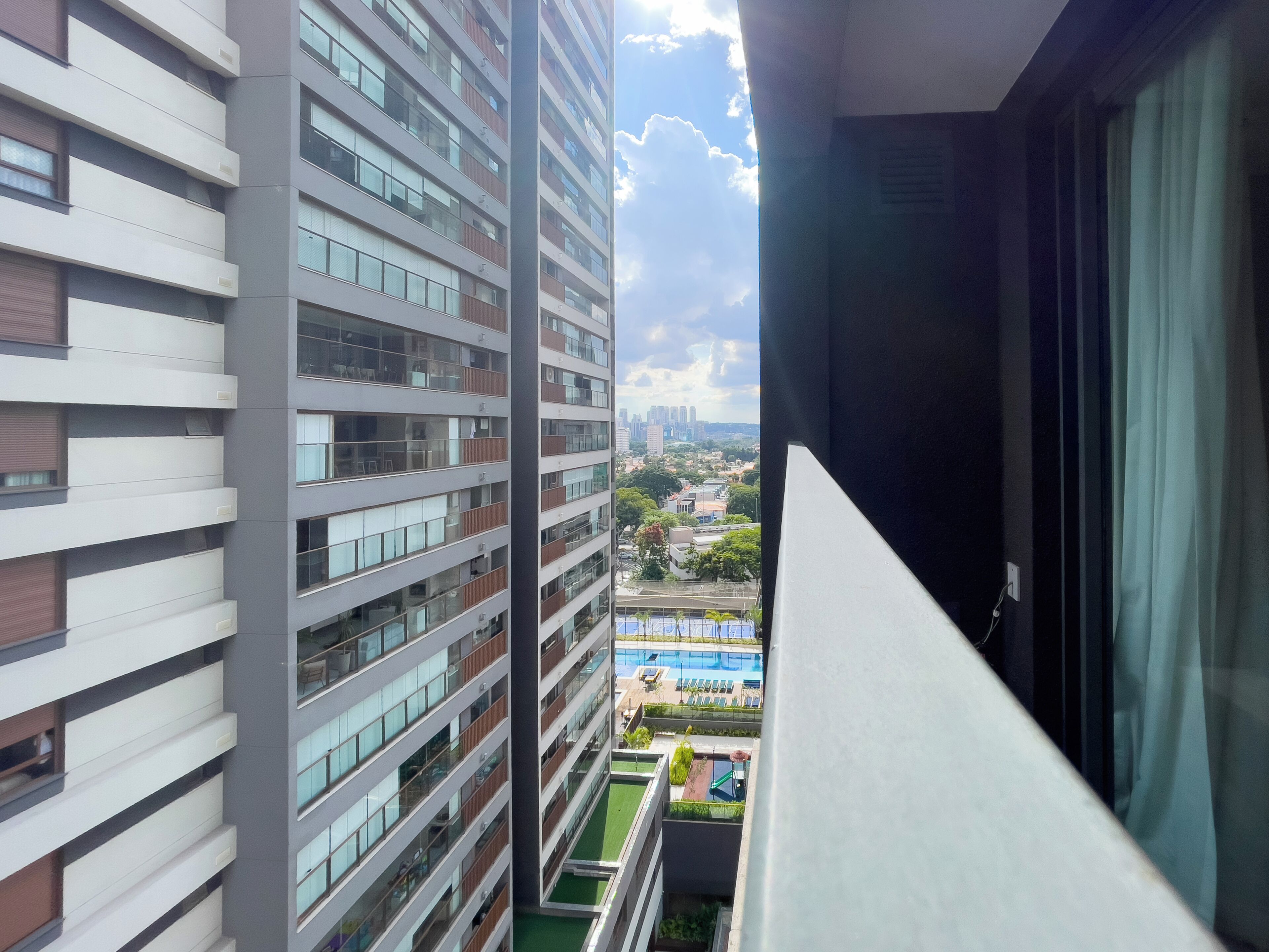 Een hoog gebouw met meerdere verdiepingen, grote ramen en uitzicht op een zwembad en groen onder het gebouw.