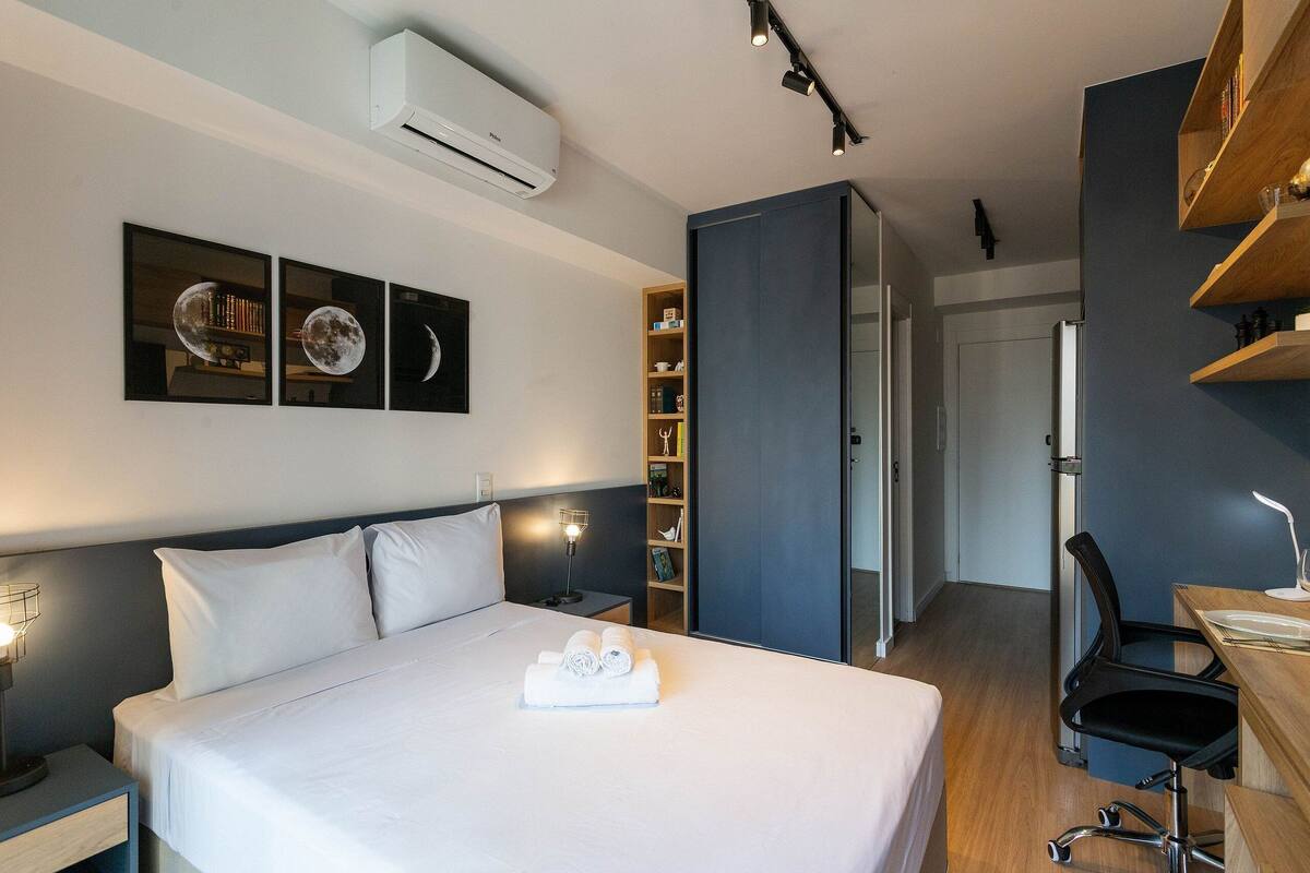 Een hotelkamer met een bed, nachtkastjes, een bureau met stoel, een boekenkast en een deur naar een andere kamer.