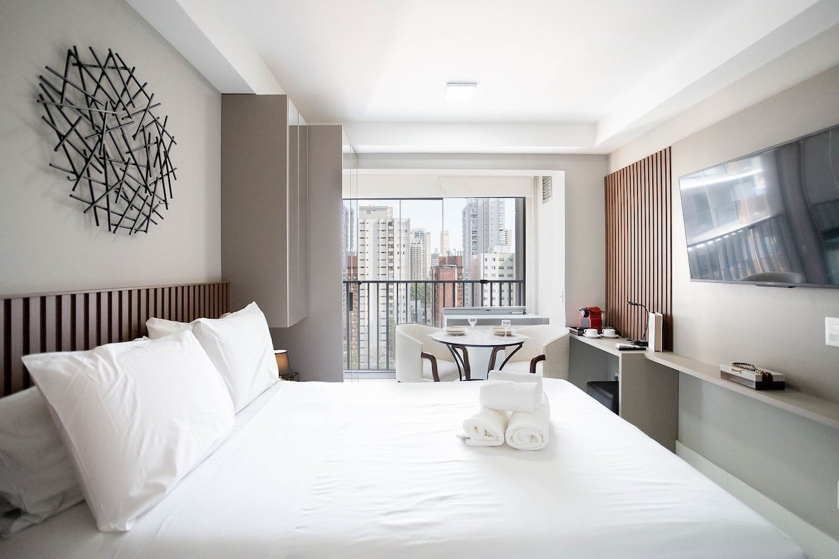 Een moderne hotelkamer met een groot bed, een eettafel en een balkon met uitzicht over de stad.