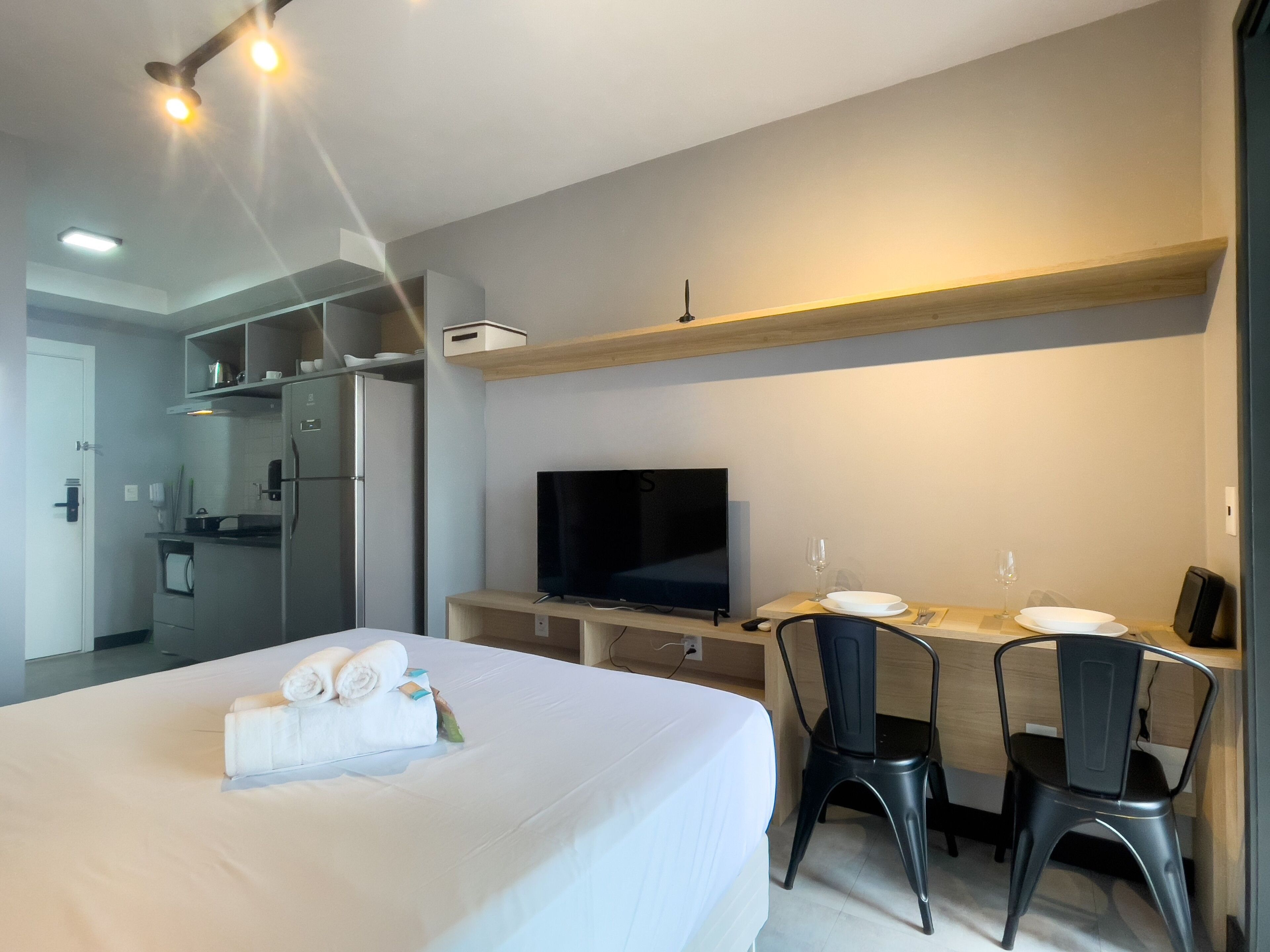 A hotel room with a bed, a desk with two chairs, a television, and a kitchenette.