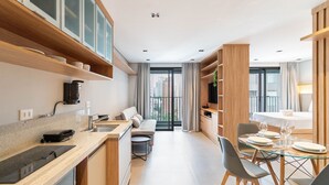 A modern kitchen with a built-in oven, a dining area with a glass table and chairs, and a sofa in the background.