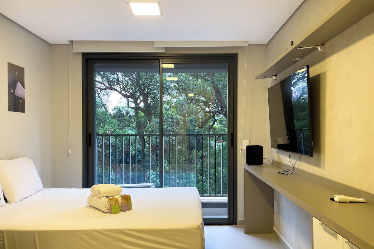 Een hotelkamer met een bed, een aan de muur bevestigde televisie en een balkon met uitzicht op bomen.