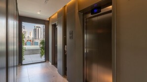 A modern elevator with a digital display, a clear glass door, and a view of a cityscape through the adjacent corridor.