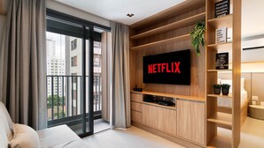 A modern living room with a large flat-screen TV mounted on a wooden wall, a sofa, and a sliding glass door leading to a balcony.