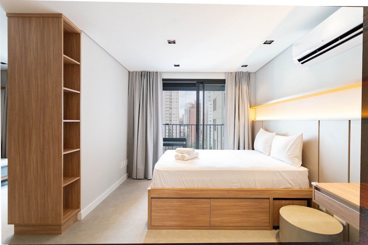 Een moderne slaapkamer met een bed, een inbouwkast en uitzicht op de stad door een groot raam.