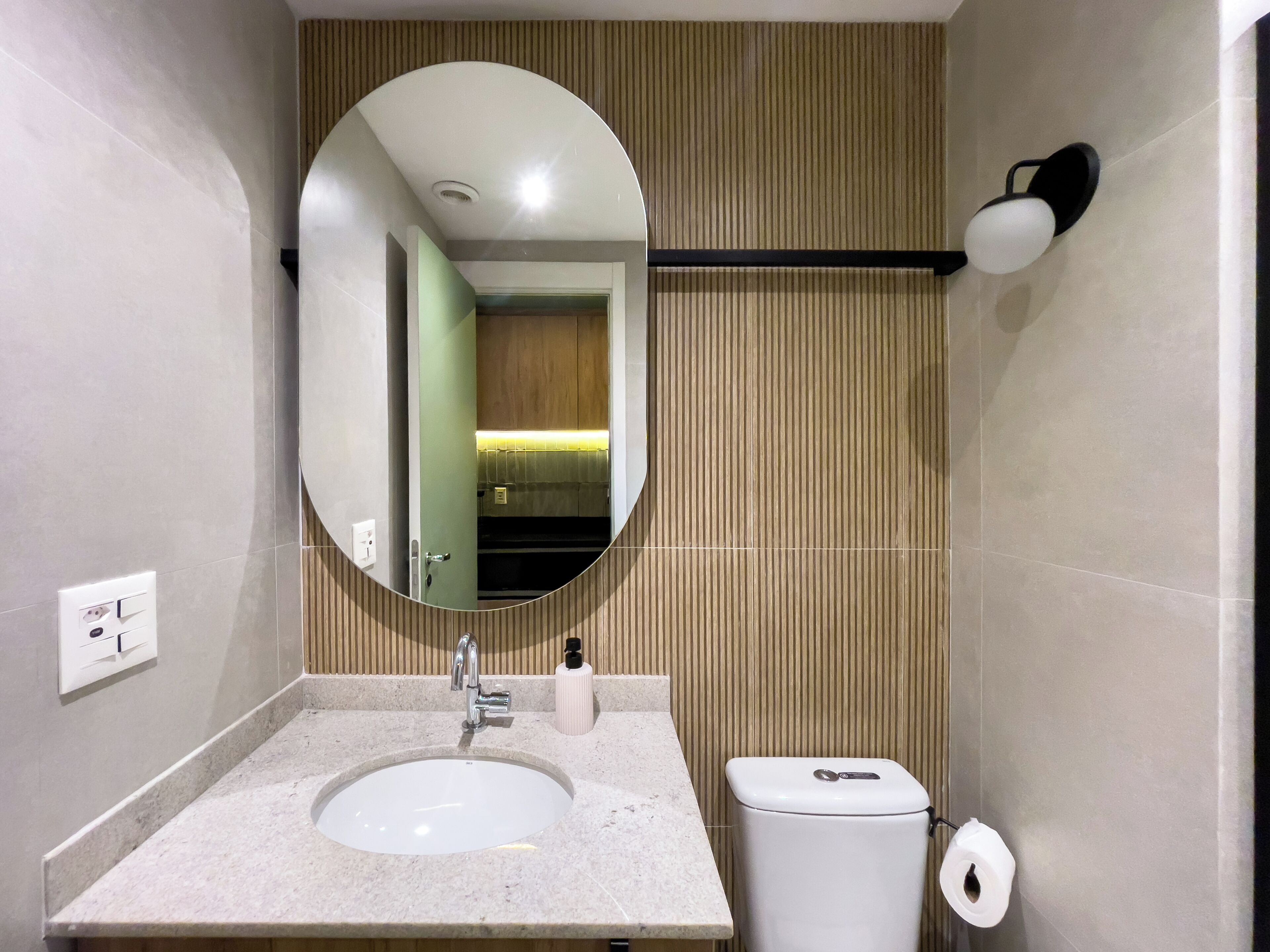 Une salle de bain moderne avec un miroir rond, un lavabo, des toilettes et un distributeur de serviettes.