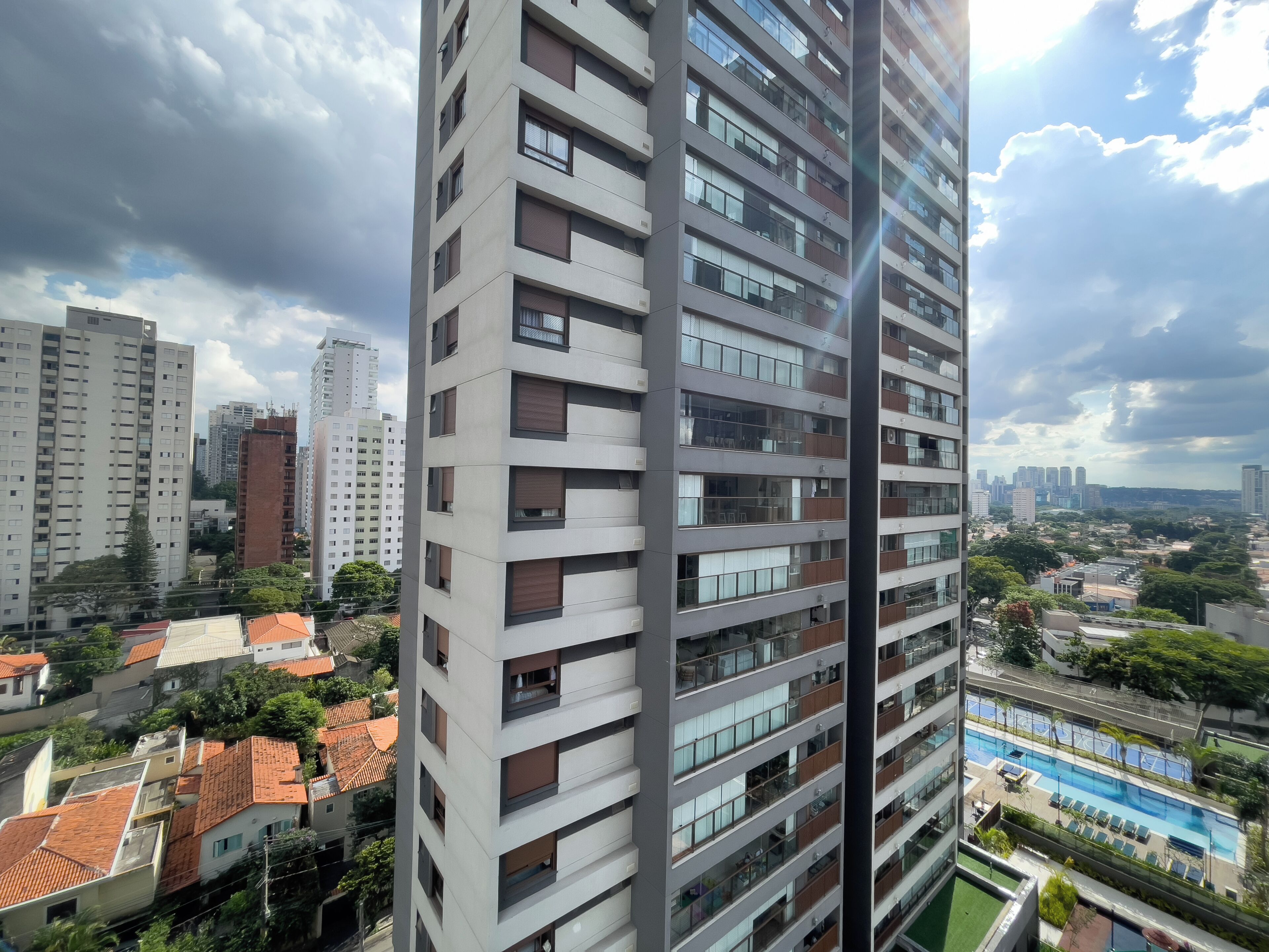 Um edifício alto com várias varandas, uma piscina e vista para a paisagem urbana ao redor.