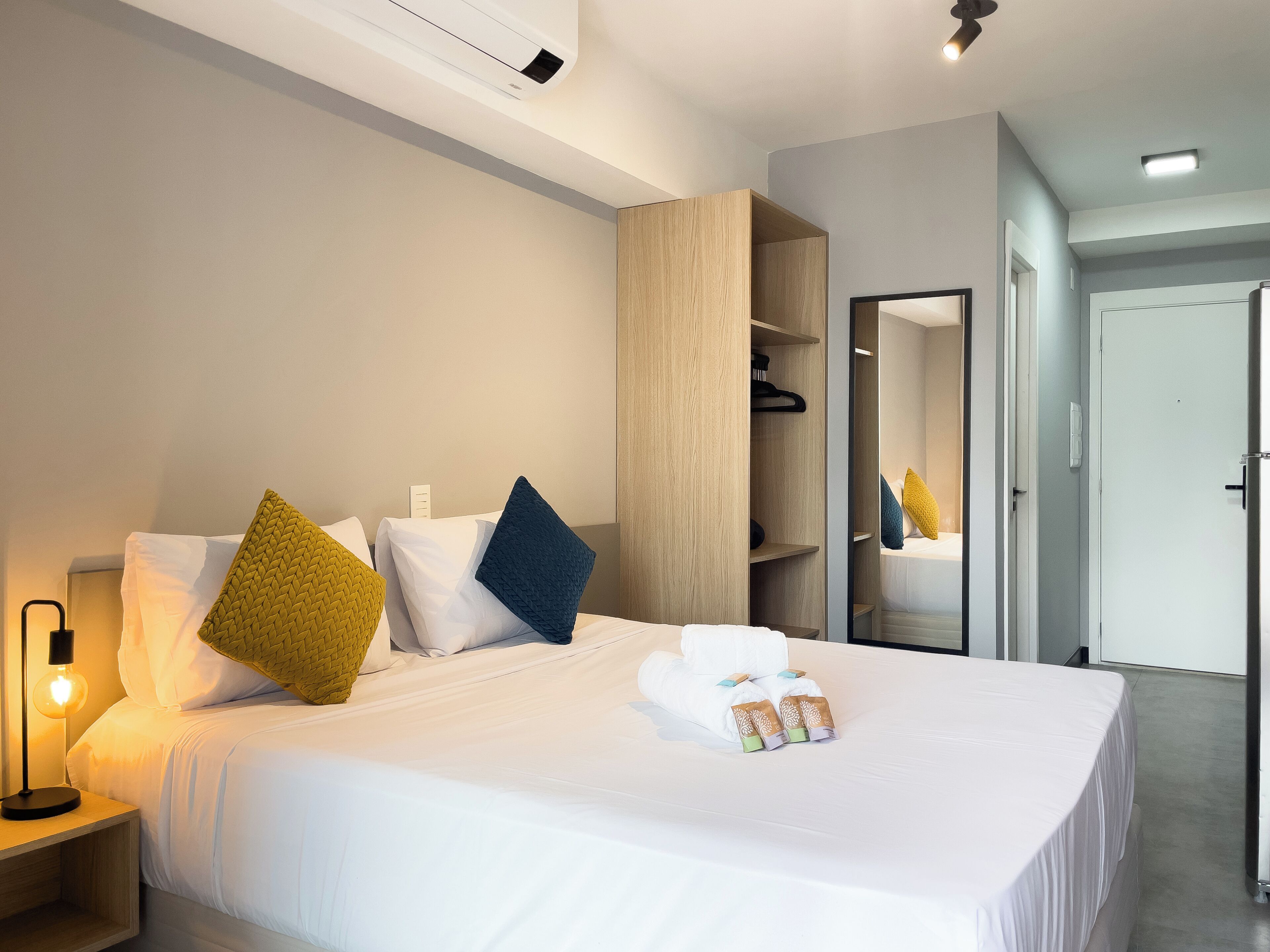 Ett modernt hotellrum med en väl bäddad säng, en sänglampa, en garderob och en spegel.
