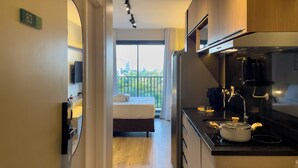 A modern hotel room with a kitchen, a bed, and a balcony with a city view.