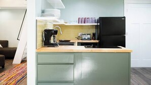 Une cuisine compacte équipée d’une cuisinière à deux brûleurs, d’une machine à café et d’un réfrigérateur noir.