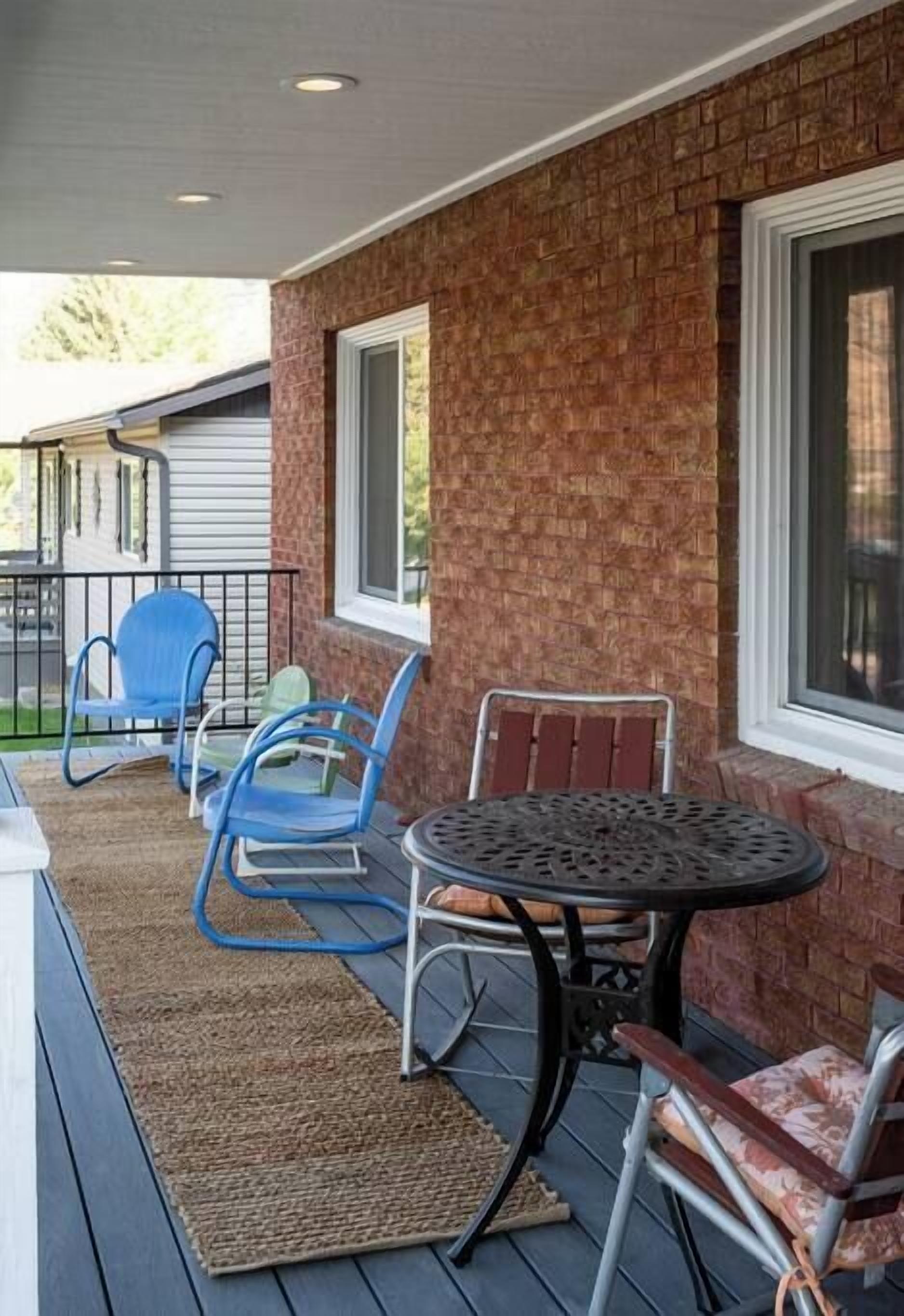 A covered patio with a brick wall, a metal table, and blue and red chairs.