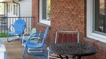 A covered patio with a brick wall, a metal table, and blue and red chairs.