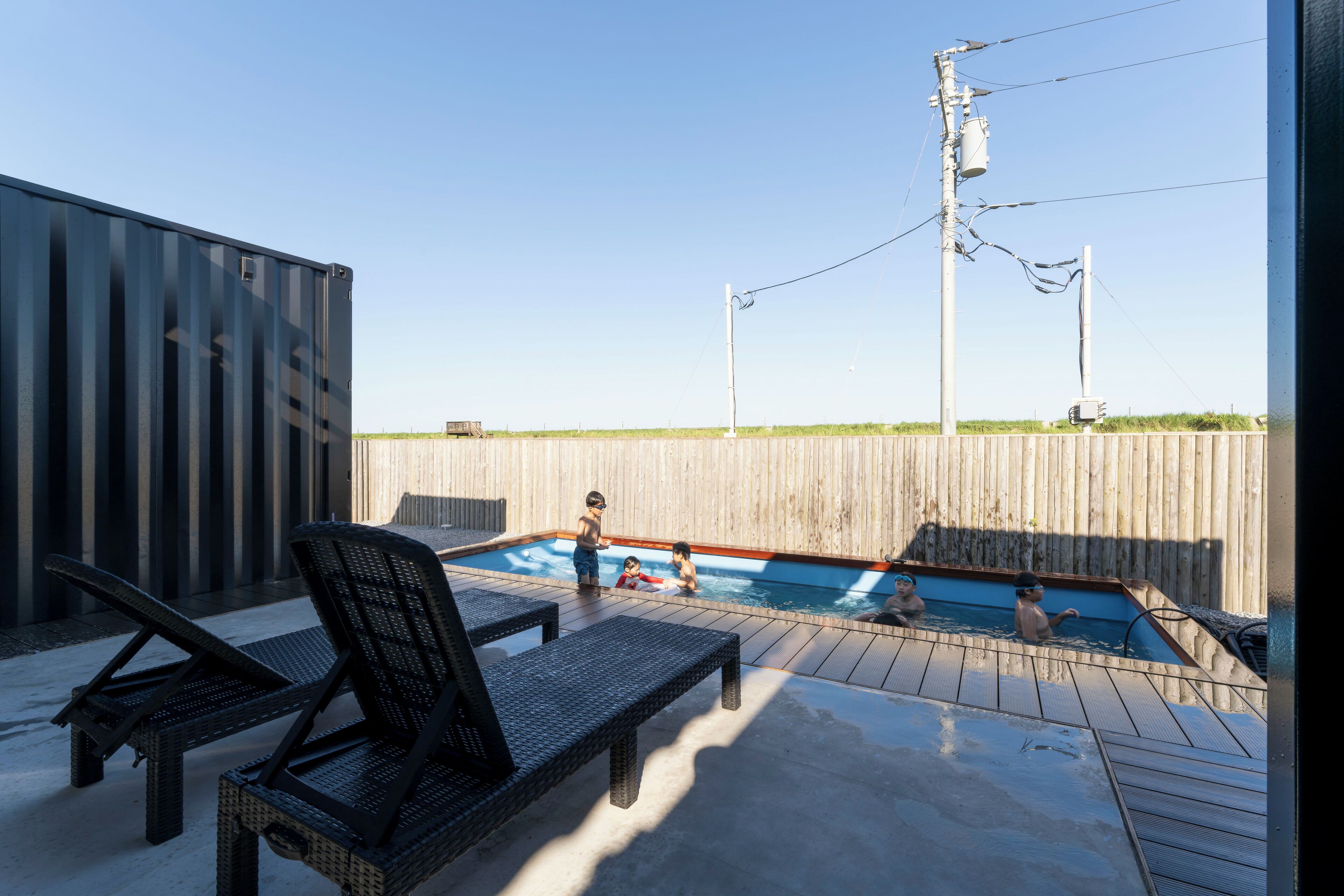 A swimming pool with lounge chairs and a wooden fence in the background.