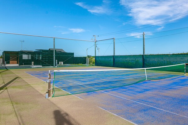 An outdoor tennis court with a net, surrounded by a fence and utility poles. - RIVIERA Kujukuri (Kujukuri)
