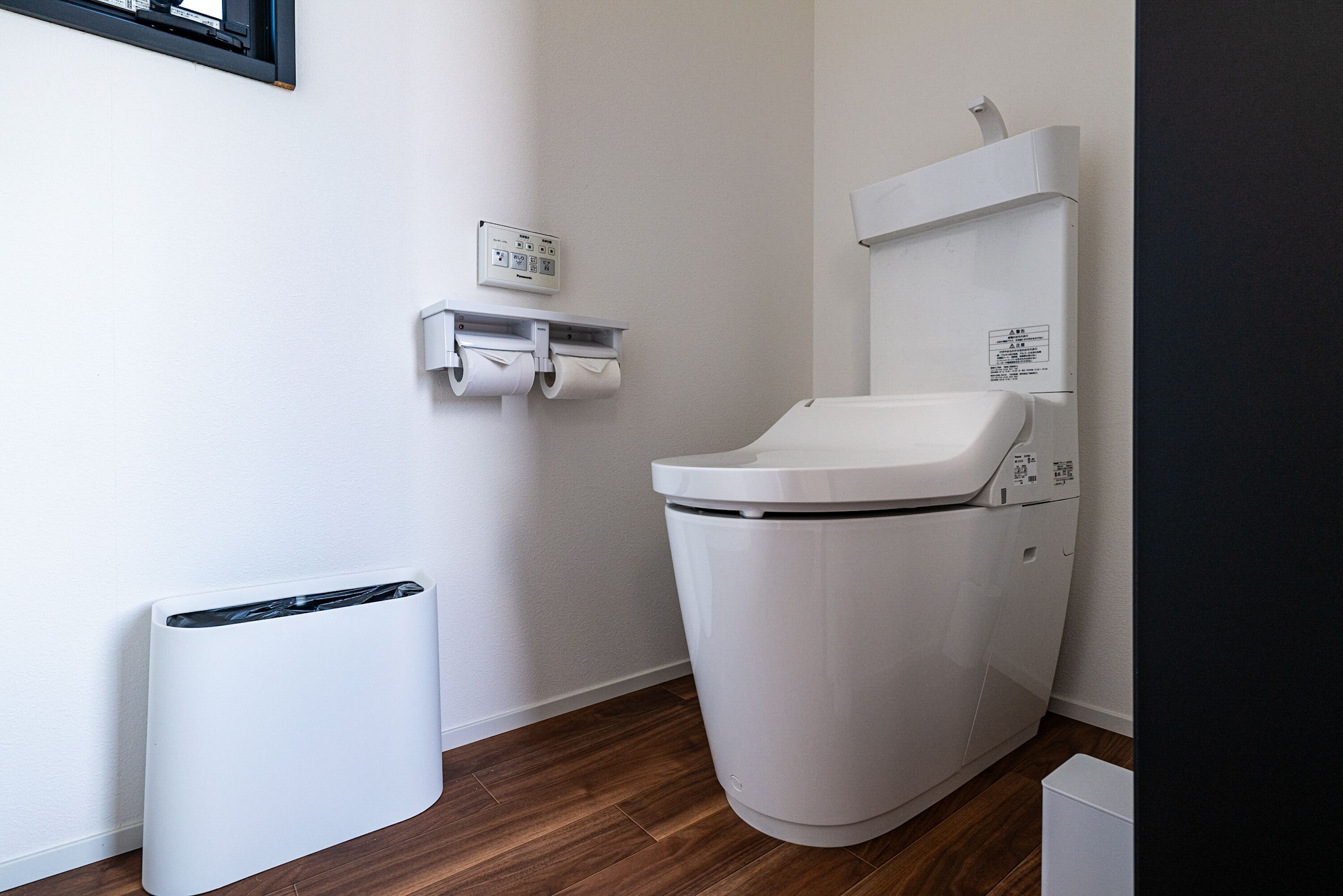 A modern bathroom with a toilet, a trash bin, and a paper towel dispenser.