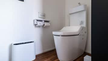 A modern bathroom with a toilet, a trash bin, and a paper towel dispenser.