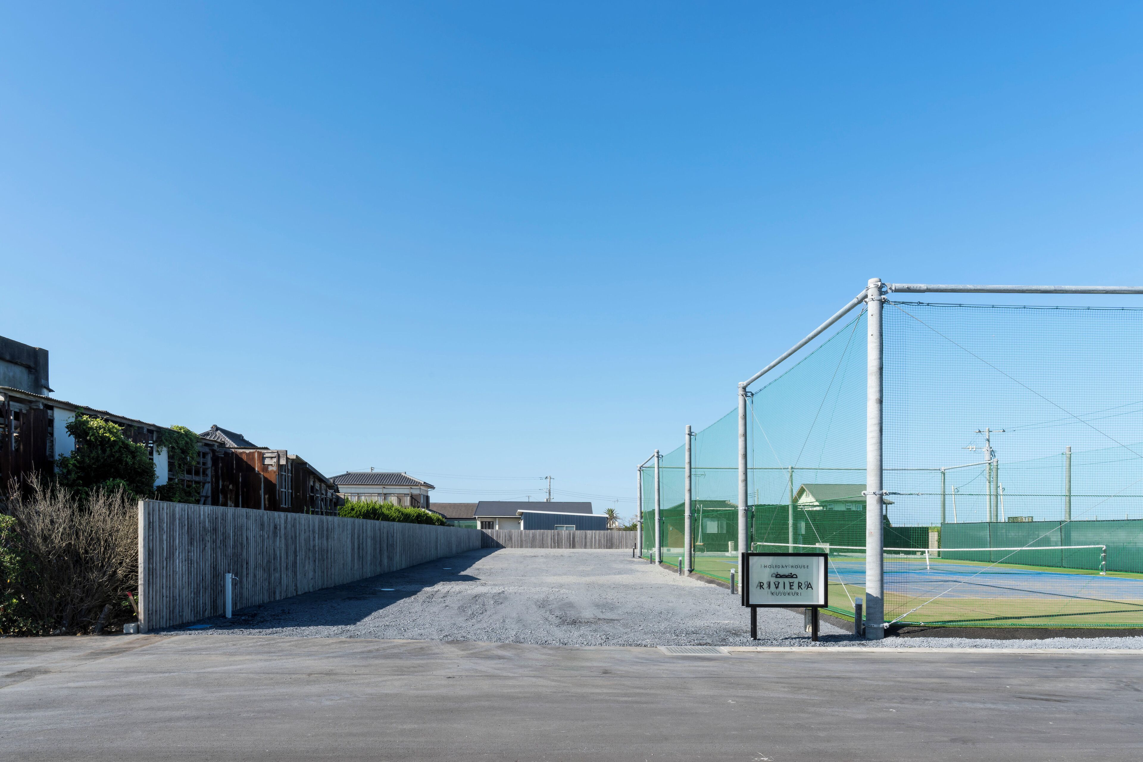 Un court de tennis avec un filet, entouré d’une clôture, et un panneau indiquant qu’il fait partie d’un parcours de golf.