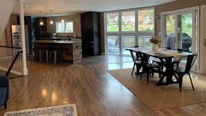 Uma cozinha ampla com ilha central, área de jantar com mesa e cadeiras, e uma grande porta de vidro deslizante que dá para um deck.