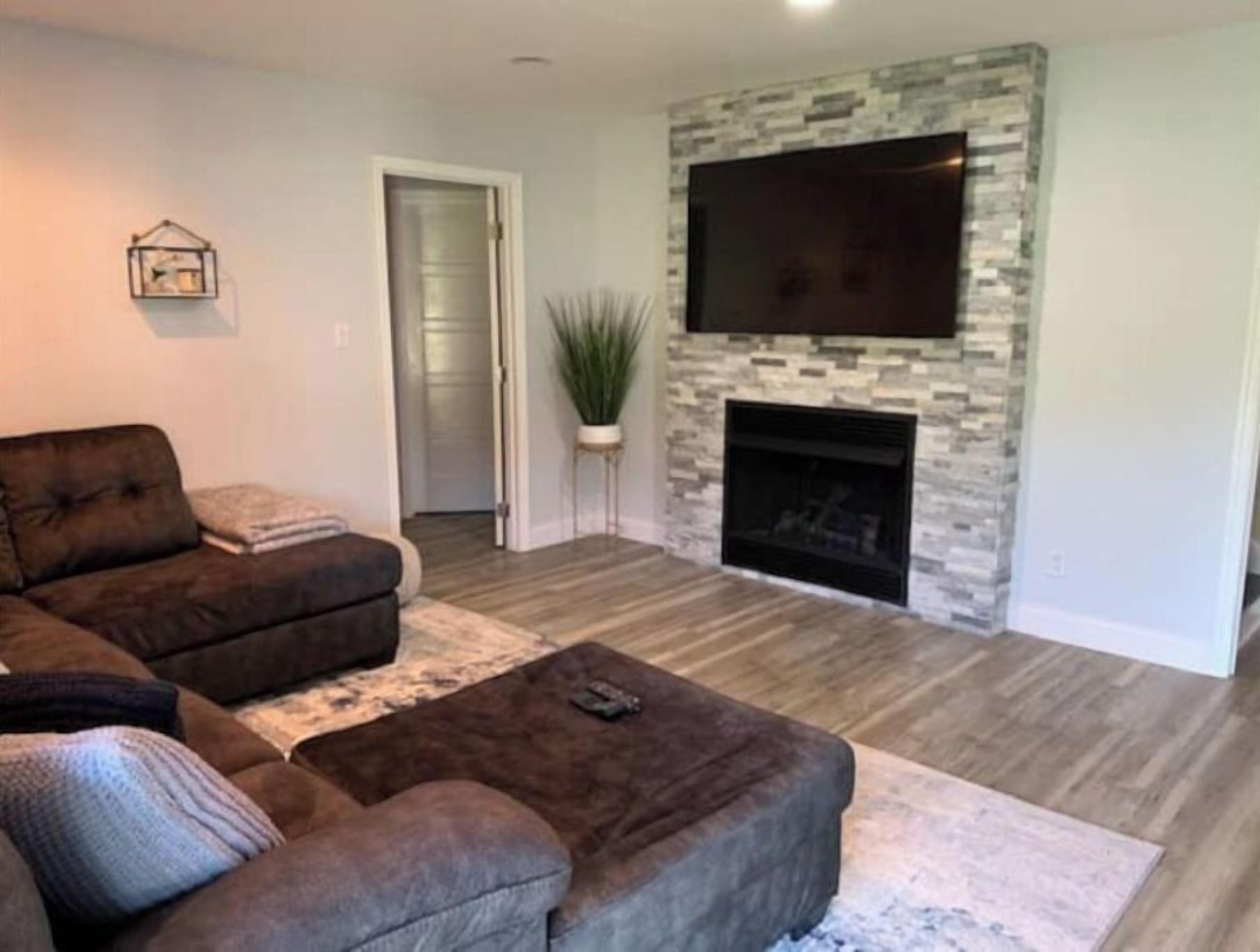 A living room with a sectional sofa, a fireplace, and a flat-screen TV mounted on a stone wall.
