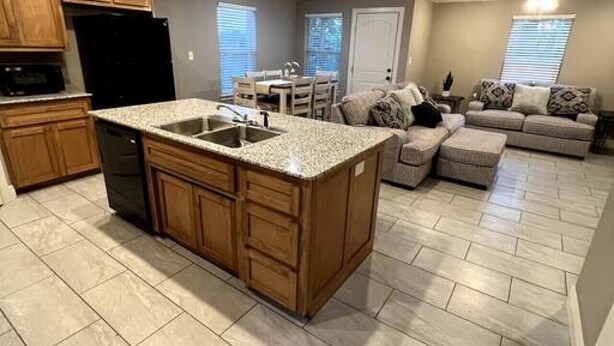 A spacious kitchen with a large island, wooden cabinets, and a black refrigerator. - New Luxury 3 Bed 2 1/2 Bath Duplex (Barling)