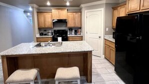 A modern kitchen with a central island, wooden cabinets, and a black refrigerator. - New Luxury 3 Bed 2 1/2 Bath Duplex (Barling)