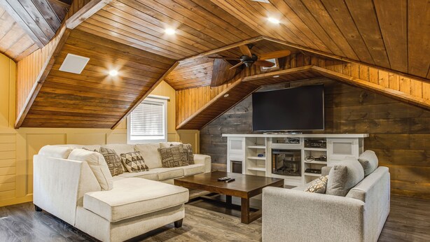 A cozy loft-style living room with wooden beams, a fireplace, and a flat-screen TV. - Amazing Lakeview Retreat with Hot Tub, Sauna and Private Loft! (Tiny)