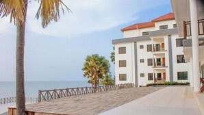 Un hôtel situé en bord de mer, doté d’une terrasse en bois, de palmiers et offrant une vue sur l’océan.