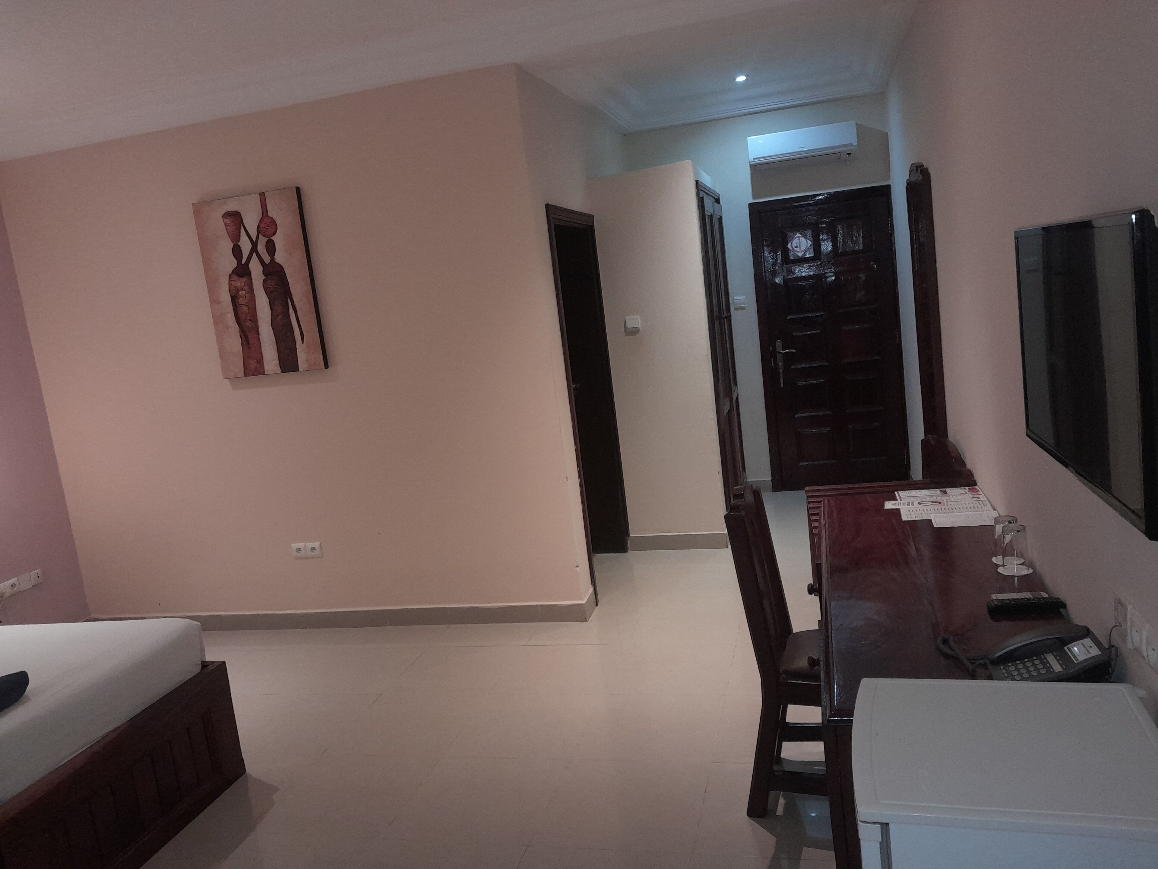 Uma sala ampla com uma mesa de jantar, uma TV fixada na parede e uma porta que dá para outro quarto.