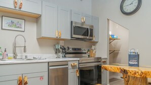 Uma cozinha moderna com armários cinzas, eletrodomésticos de aço inoxidável, micro-ondas e uma mesa de madeira com um banco.