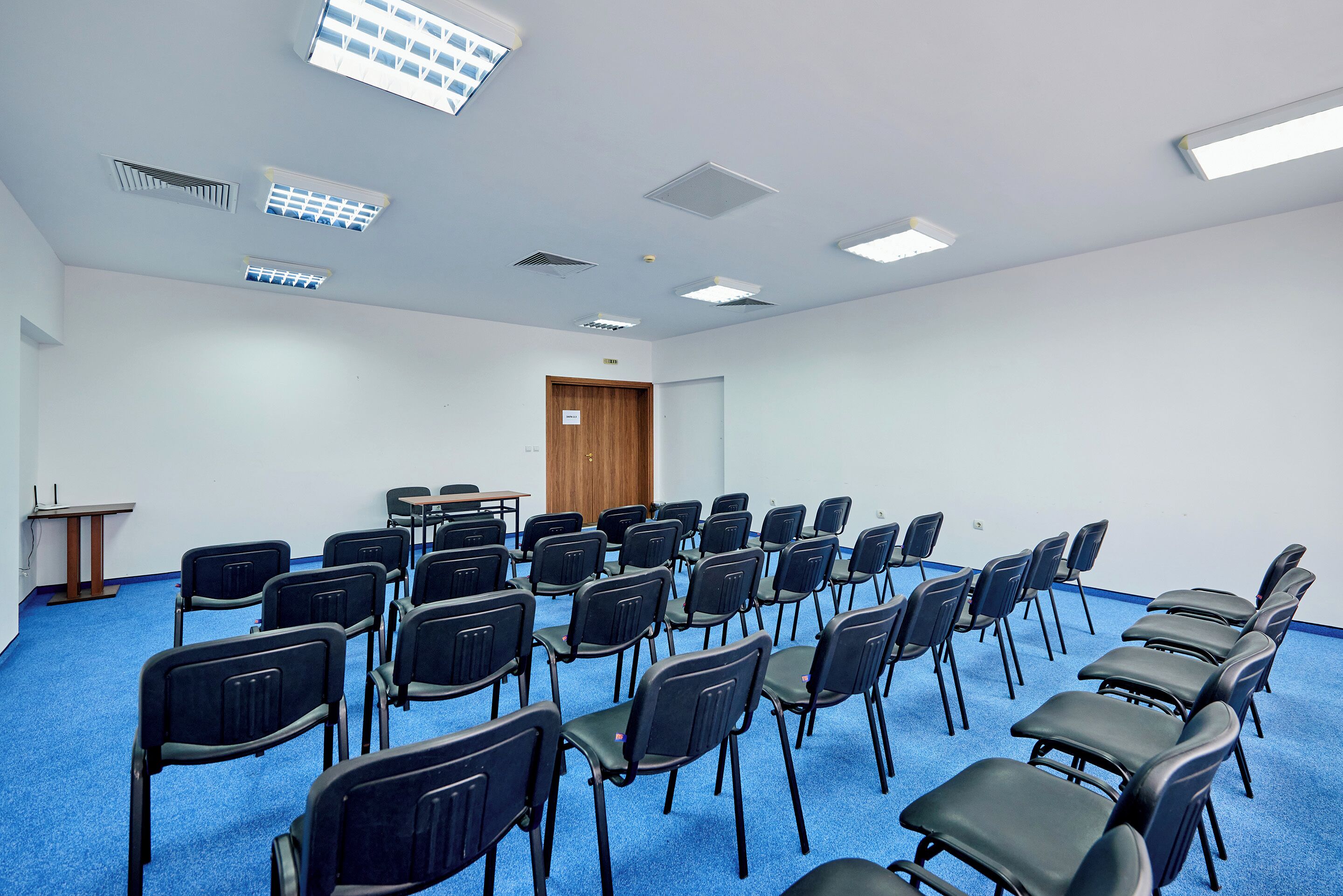 A conference room with rows of chairs, a podium, and ceiling lights.