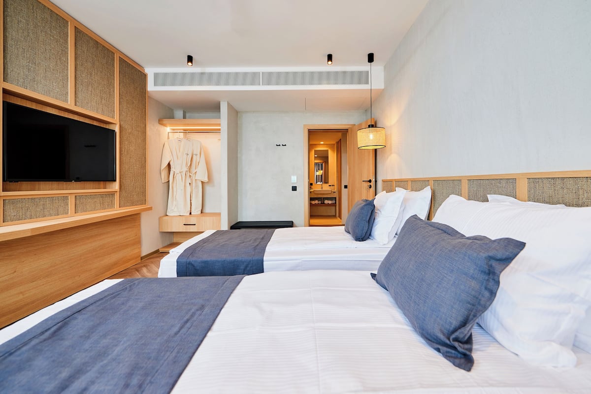 A hotel room with two beds, a TV, a robe, and a bathroom visible through an open door.