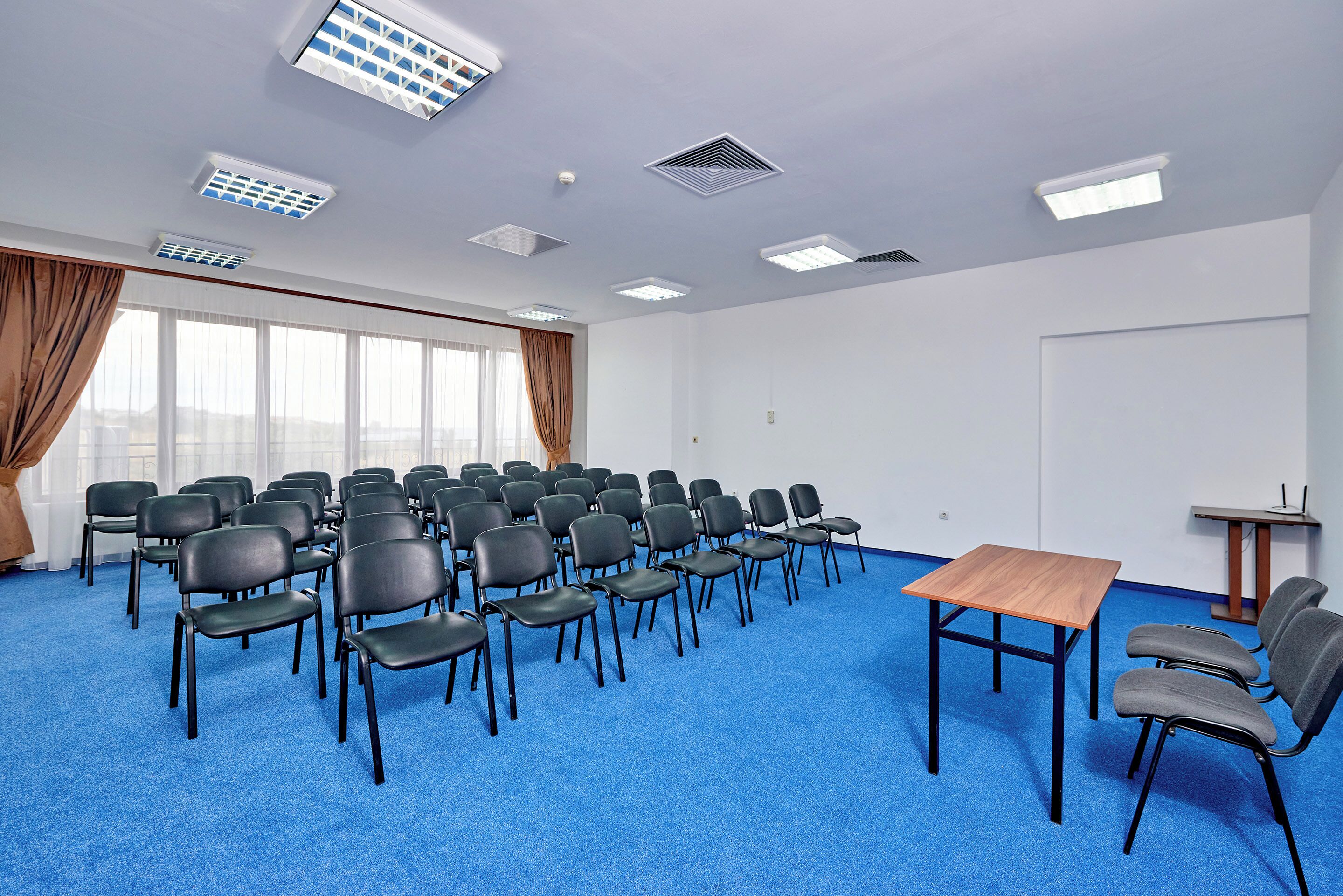 A conference room with rows of chairs, a wooden table, and a projector screen.