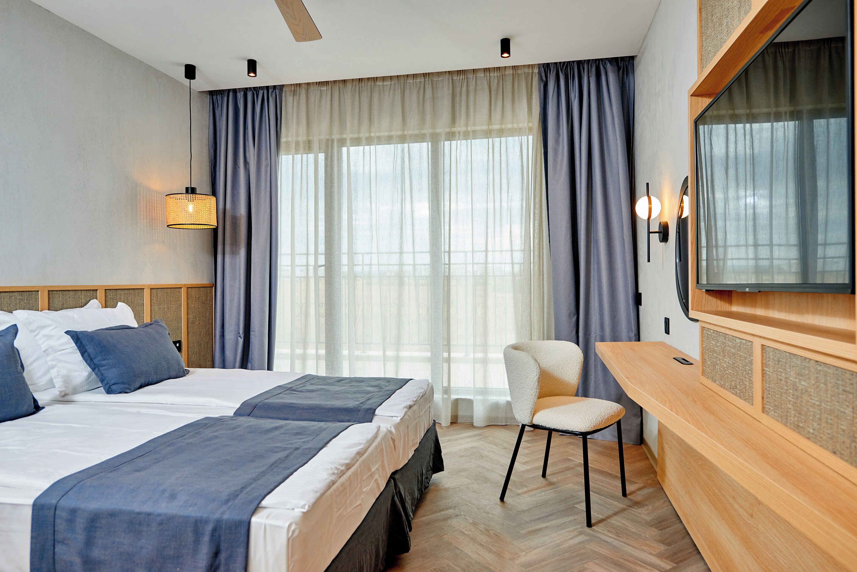 A hotel room with a large bed, a desk, a chair, and a TV.