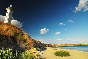 A coastal scene with a lighthouse, sandy beach, and clear blue sky. - Fara (Pomorie)