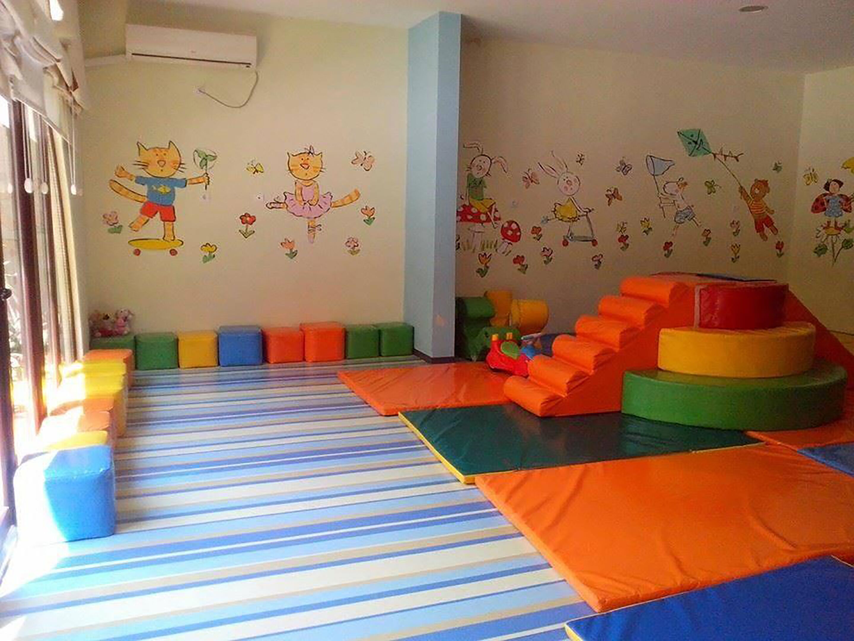Ein Kinderspielbereich mit bunten Matten, Kissen und Wanddekorationen.