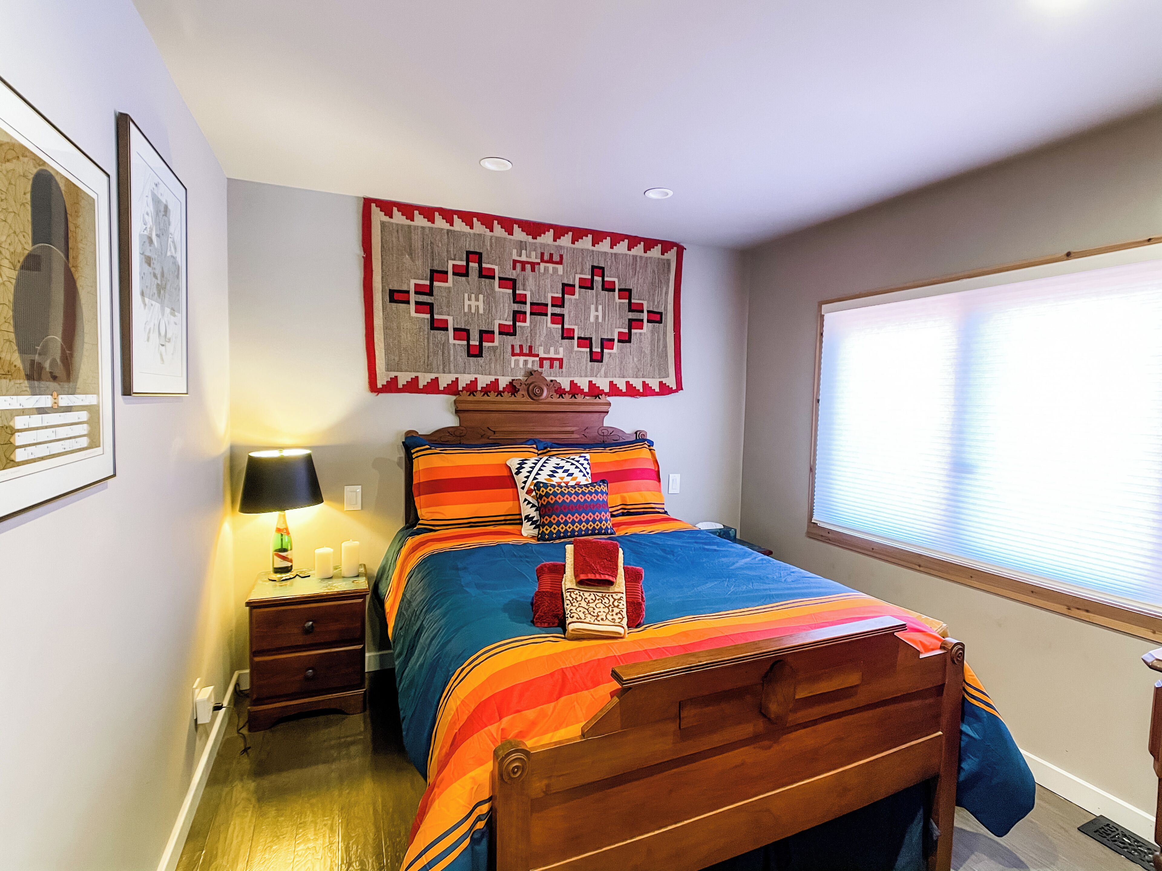 Une chambre à coucher avec un lit en bois, une table de chevet, une lampe et une fenêtre avec des stores.