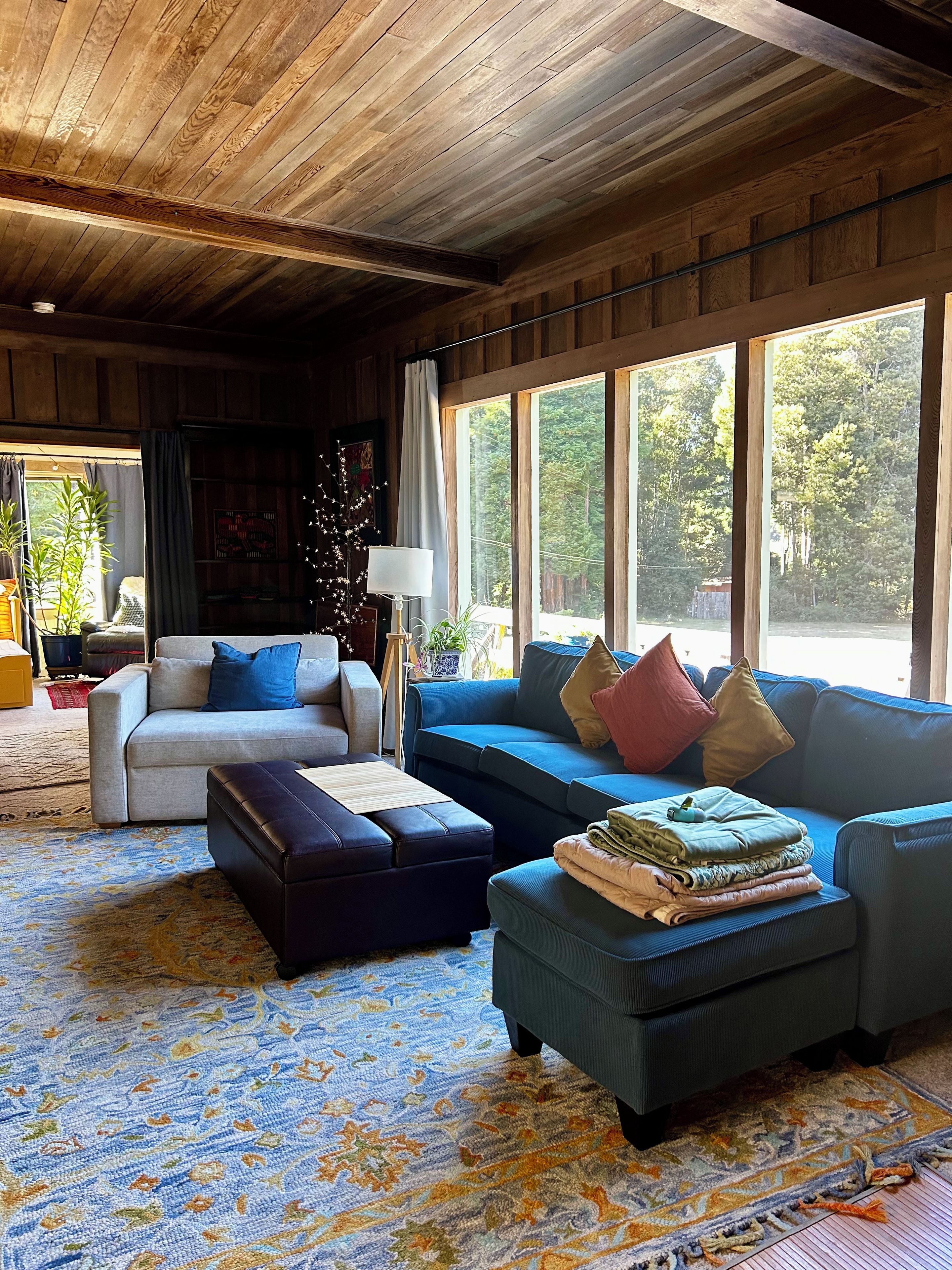 A cozy living room with a large window, a sofa, a coffee table, and a patterned rug.