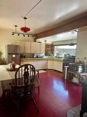 A kitchen with a red floor, wooden cabinets, a stainless steel refrigerator, and a dining area with a wooden chair. - Ranch home w/ hot tub in the Mendocino Redwoods. Pet- & family-friendly. (Fort Bragg)