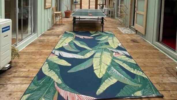 Un espace extérieur abrité, équipé d’une table de ping-pong et d’un tapis orné de motifs de feuilles tropicales.