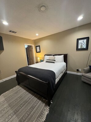 A bedroom with a bed, a bedside table, a lamp, a chair, and a door.