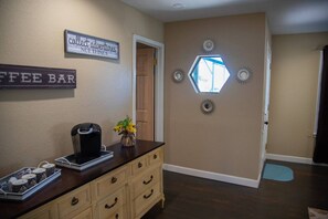 A hallway with a coffee bar sign, a coffee machine, and a vase with flowers.