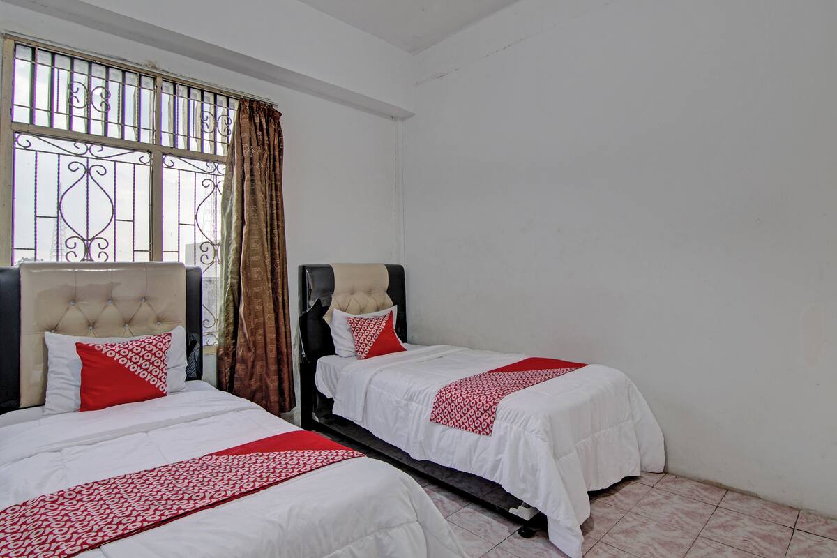 Une chambre d’hôtel avec deux lits, chacun doté d’une tête de lit capitonnée, de draps blancs et d’une couvre-lit à motifs rouges et blancs.
