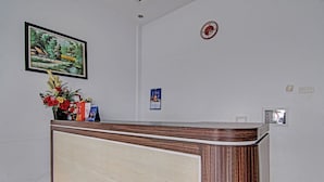 A reception desk with a framed landscape painting, a floral arrangement, and a clock on the wall.