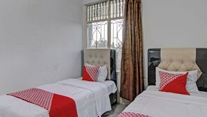 A hotel room with two beds, each with white bedding and red accents, a window with metal bars, and a curtain.